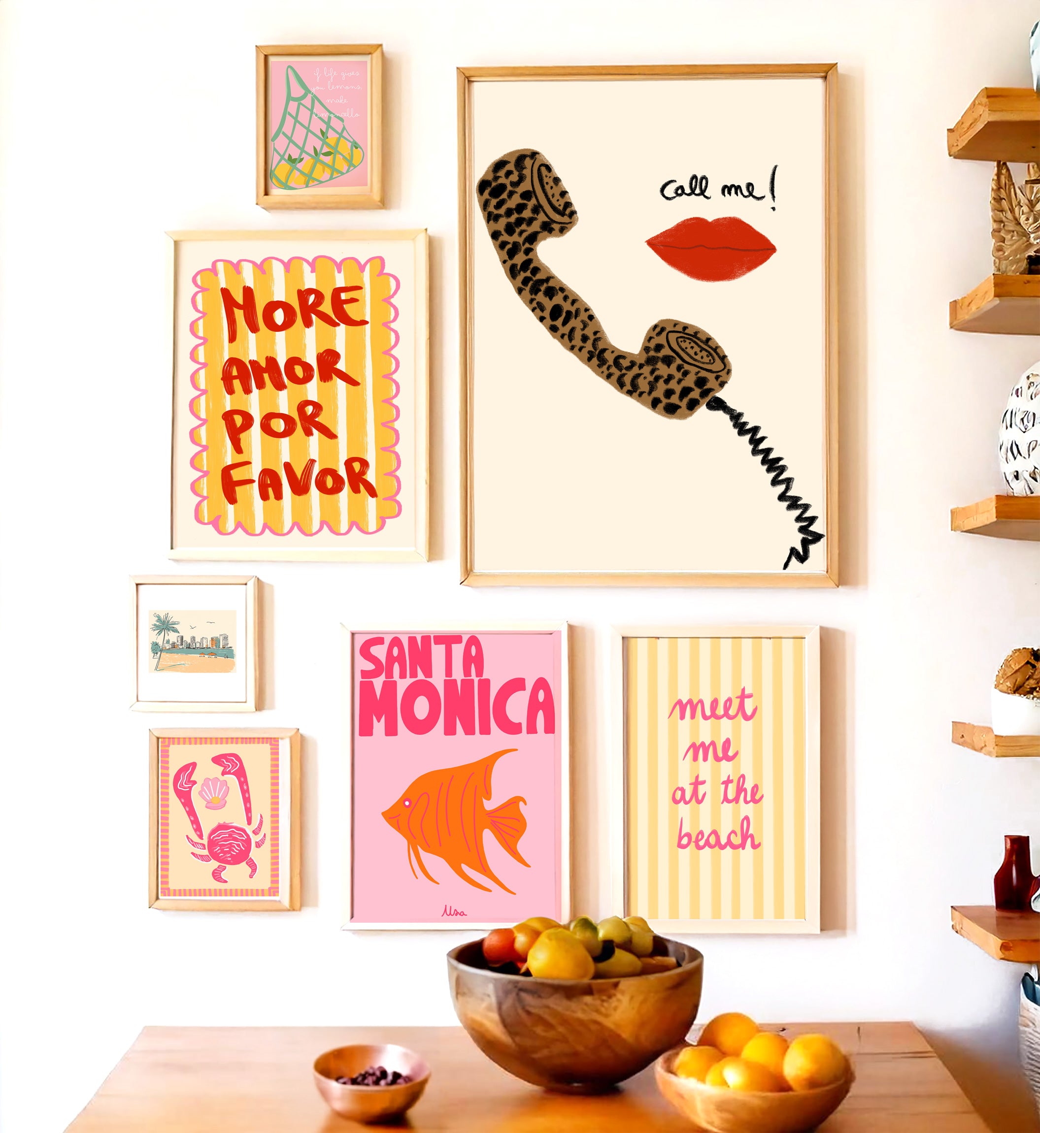 Wall with framed art prints and a bowl of fruit on a table.
